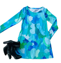 Blue and green patterned long-sleeve shirt with black boots and pink earrings on a white surface