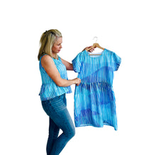 Woman holding a blue and white striped dress on a hanger against a plain background