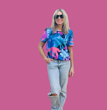 Woman wearing a colorful abstract patterned shirt and light jeans against a plain background