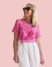 Woman wearing a pink and white striped top and white pants indoors.