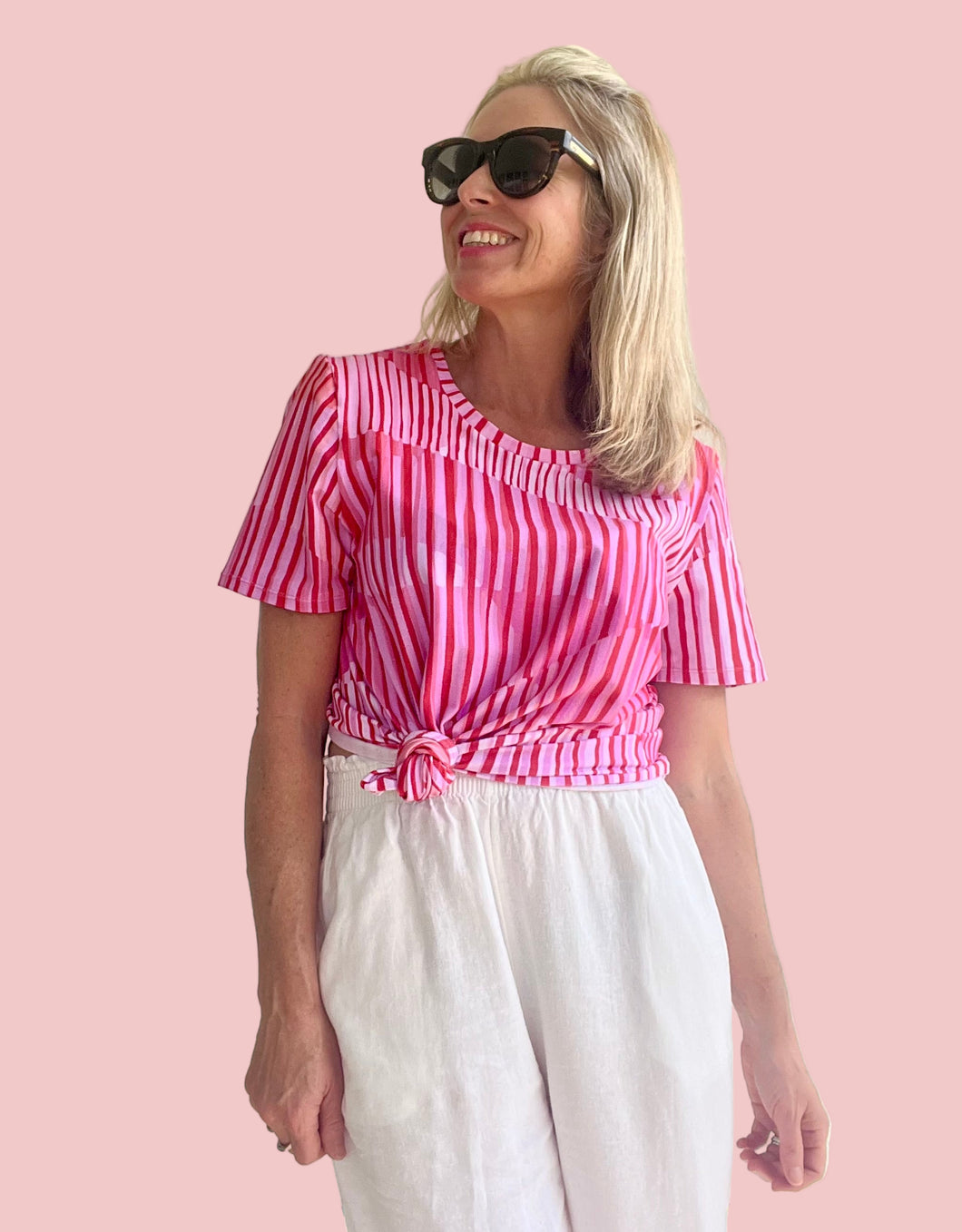 Woman wearing a pink and white striped top and white pants indoors.